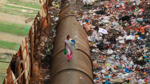 The effects of globalisation is often poverty. A woman walks on a pipe separating a row of houses and trash piles in India